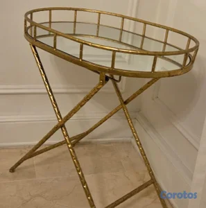 Mesa auxiliar ovalada con estructura dorada y tope de espejo.
